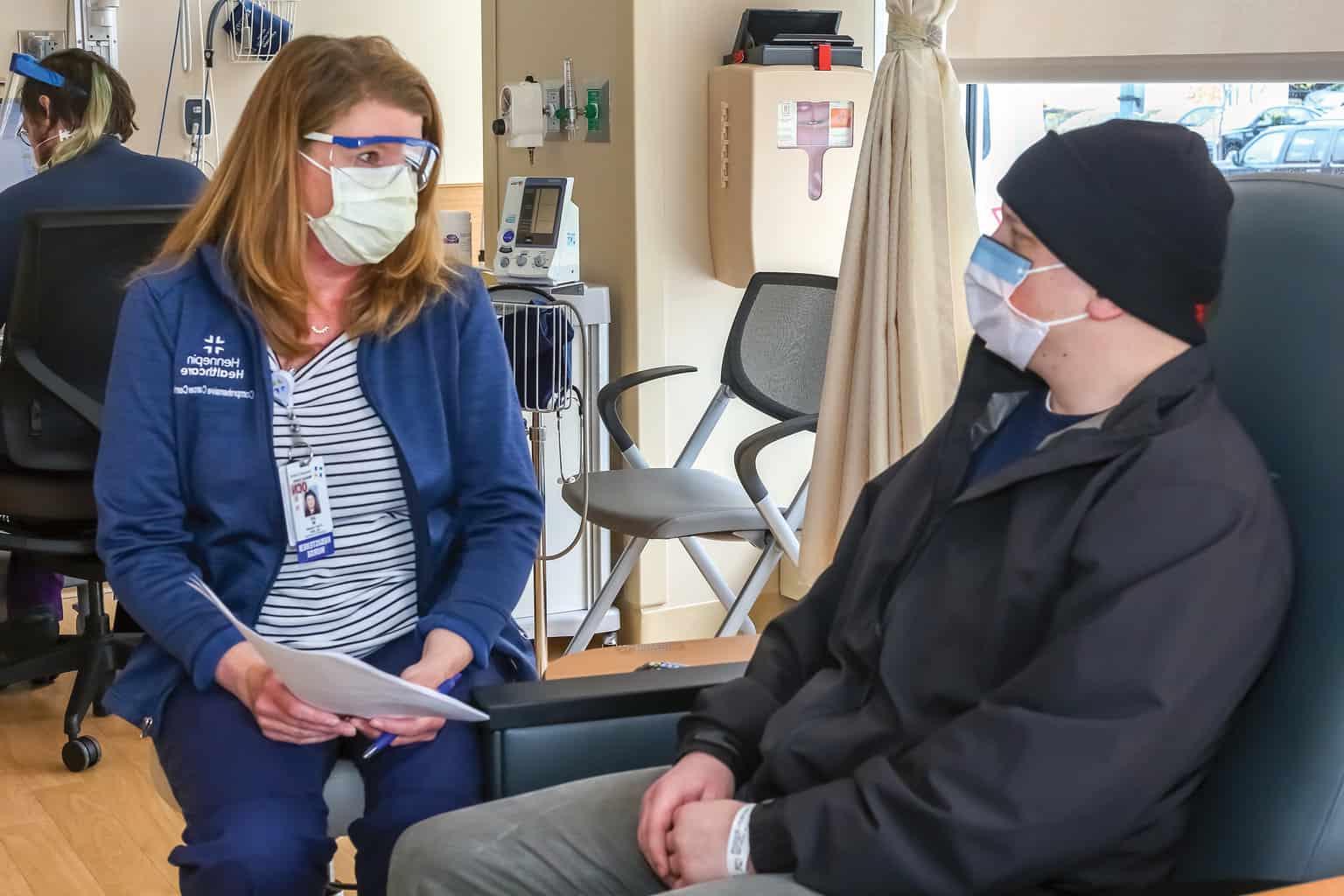 seated nurse talking to male patient in cancer center wearing masks, patient advocates, office of the patient experience, patient support, patient information, patient resources