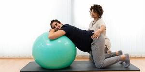 一位孕妇在理疗师的帮助下，在健身球上做呼吸练习和休息